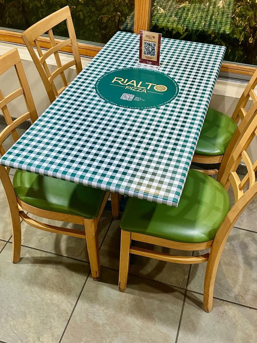 A dining table with a green and white checkered tablecloth and four green-padded chairs.