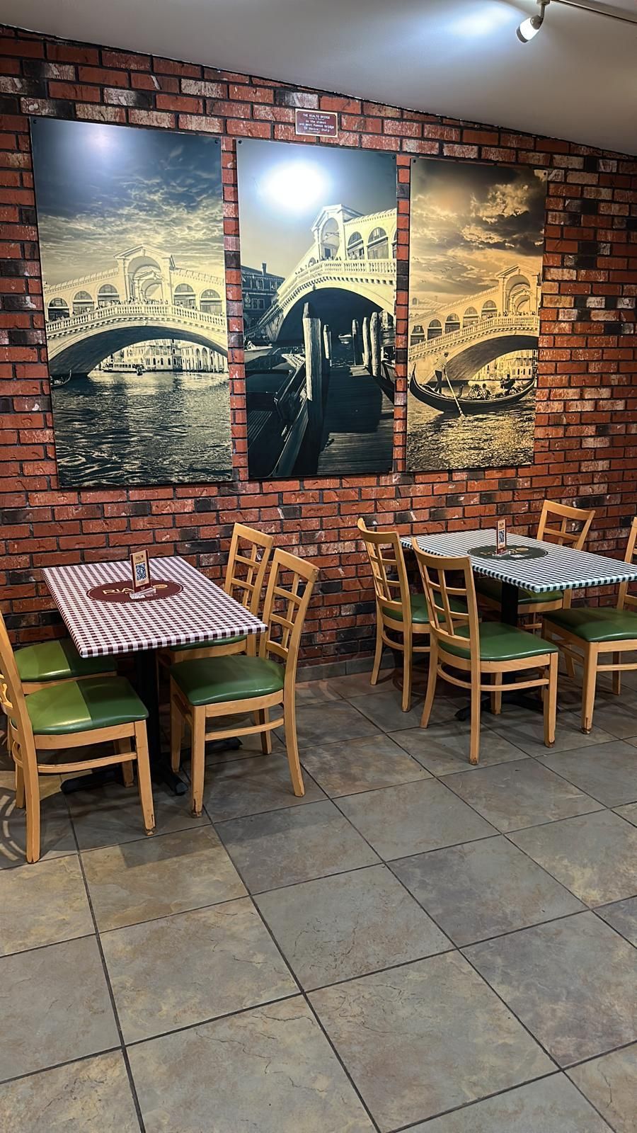 Restaurant interior with brick wall, framed bridge art, tables, and chairs.