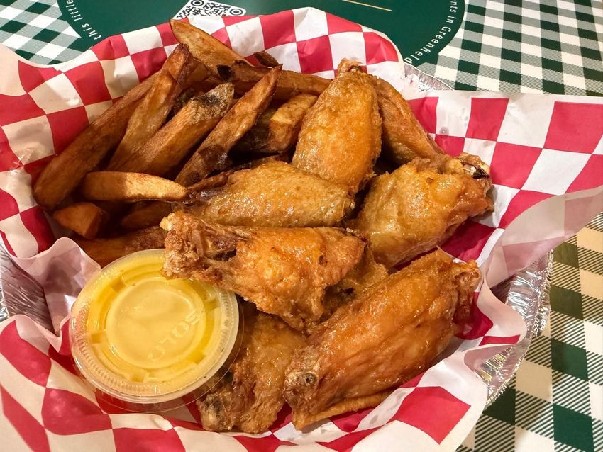 Chicken wings and fries in a checkered basket with dipping sauce.