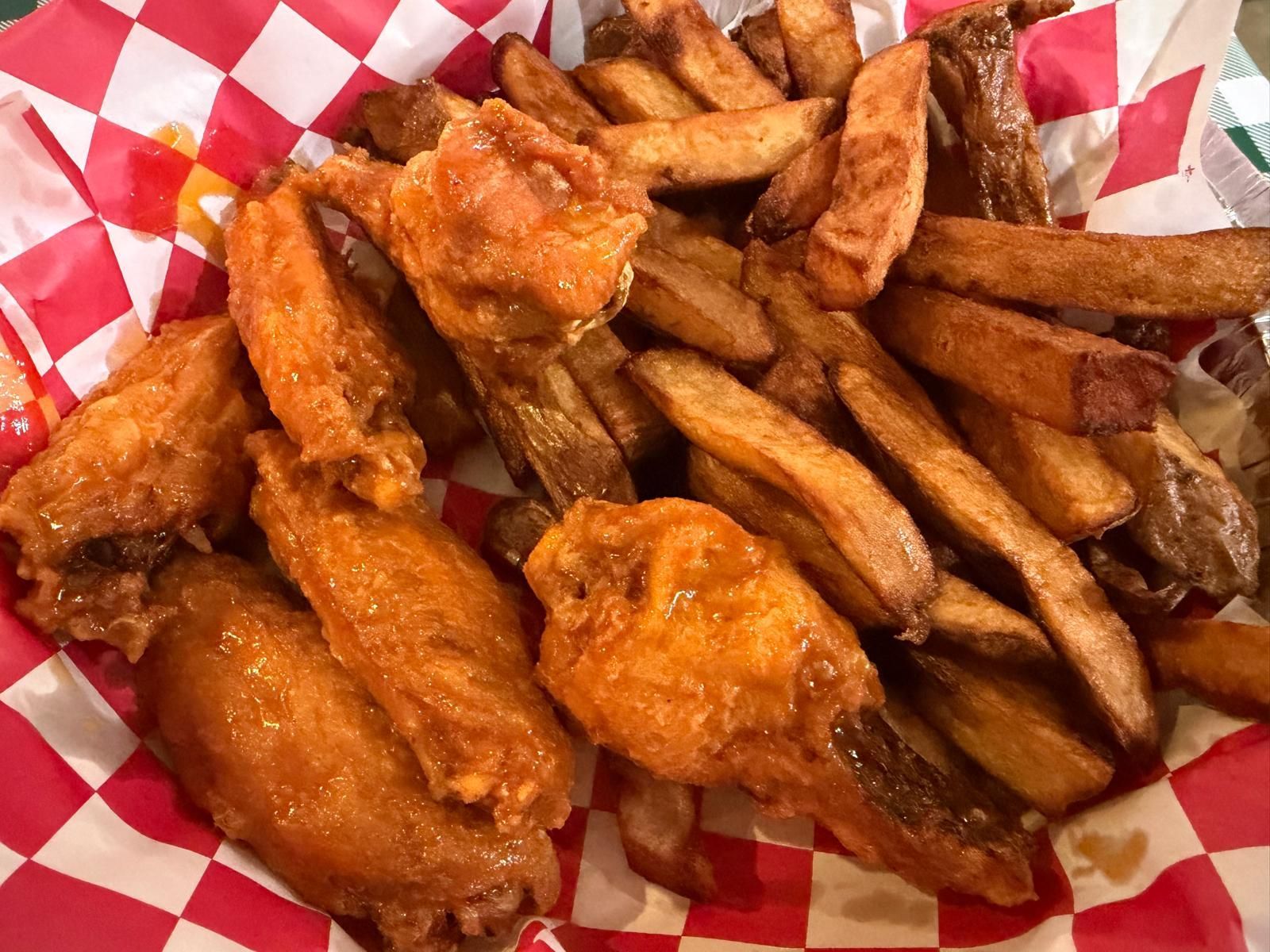 Chicken wings and fries in a red checkered basket.