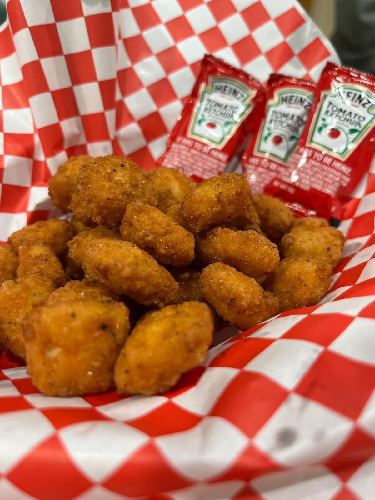 Fried potato nuggets in a red and white checkered basket with three ketchup packets.
