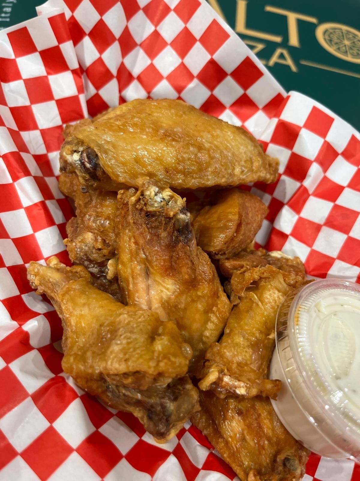 Chicken wings in red and white checkered basket, with small container of white dipping sauce.