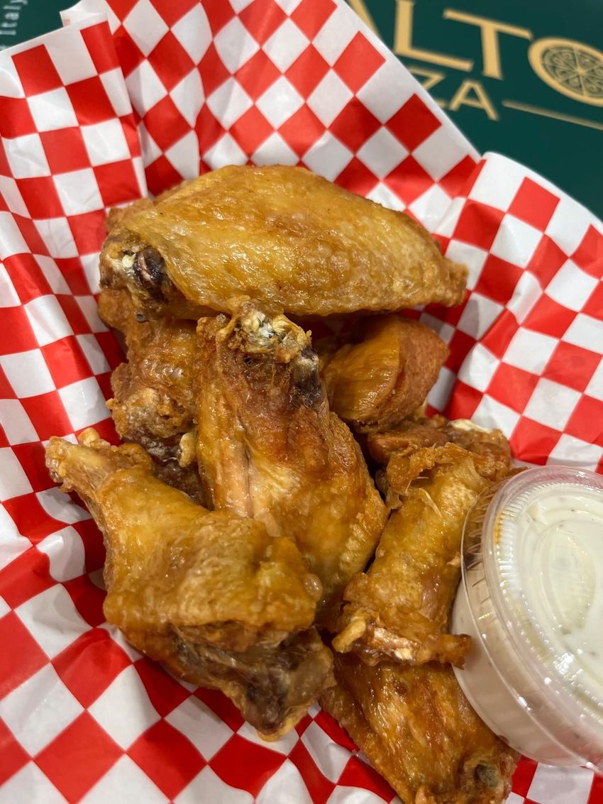 Chicken wings in red and white checkered basket, with small container of white dipping sauce.