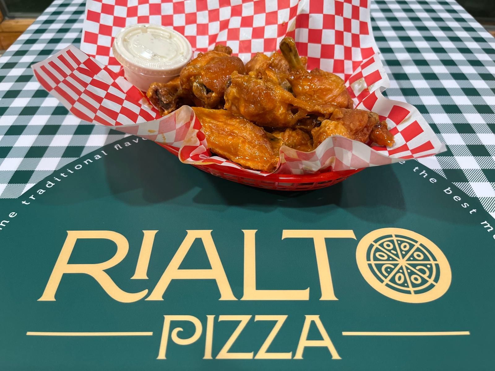 Chicken wings with dipping sauce on a table, with the Rialto Pizza logo in the foreground.
