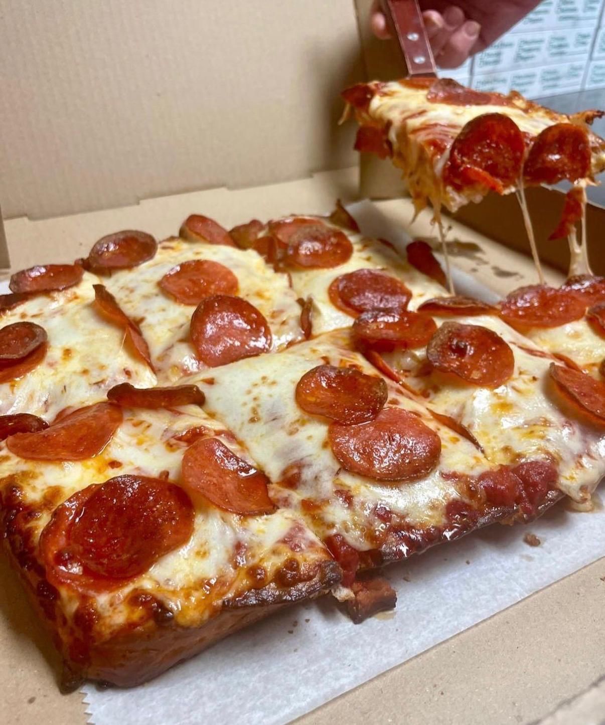 Pepperoni pizza in a box, a slice being lifted. Golden crust, melted cheese, and red pepperoni.
