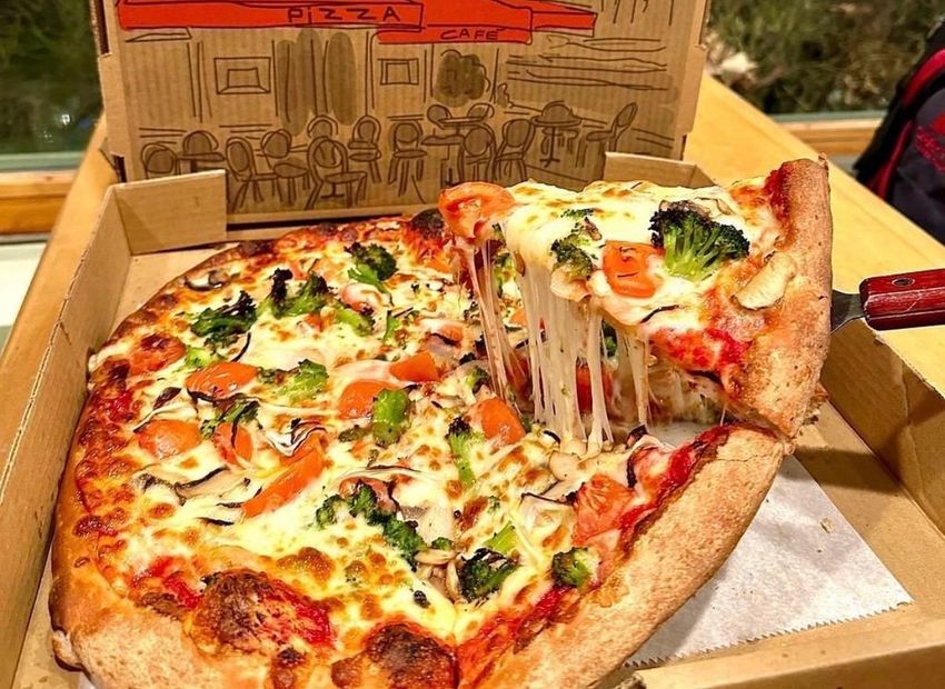 Pizza with vegetables and melted cheese, a slice being lifted from the box.