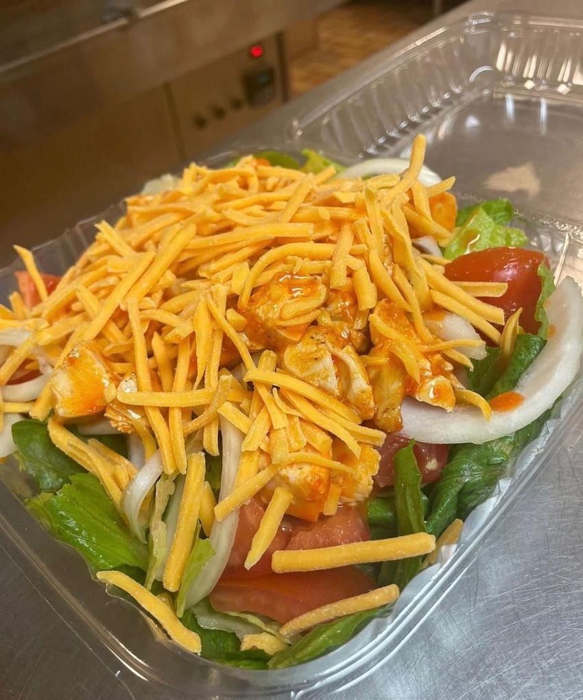 Salad in a clear container, lettuce, tomato, onion, and shredded cheddar cheese.