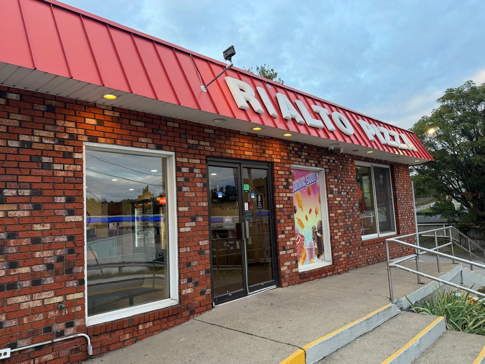 Rialto Pizza storefront with red roof and brick exterior, glass doors, and window displaying colorful images.