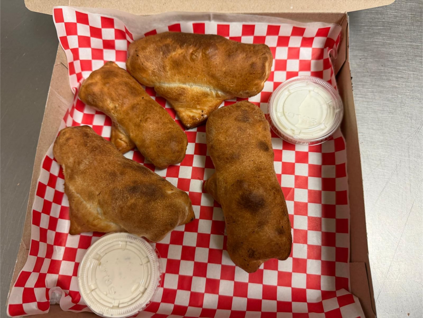 Four breaded, filled rolls in a checkered box with two small containers of white sauce.