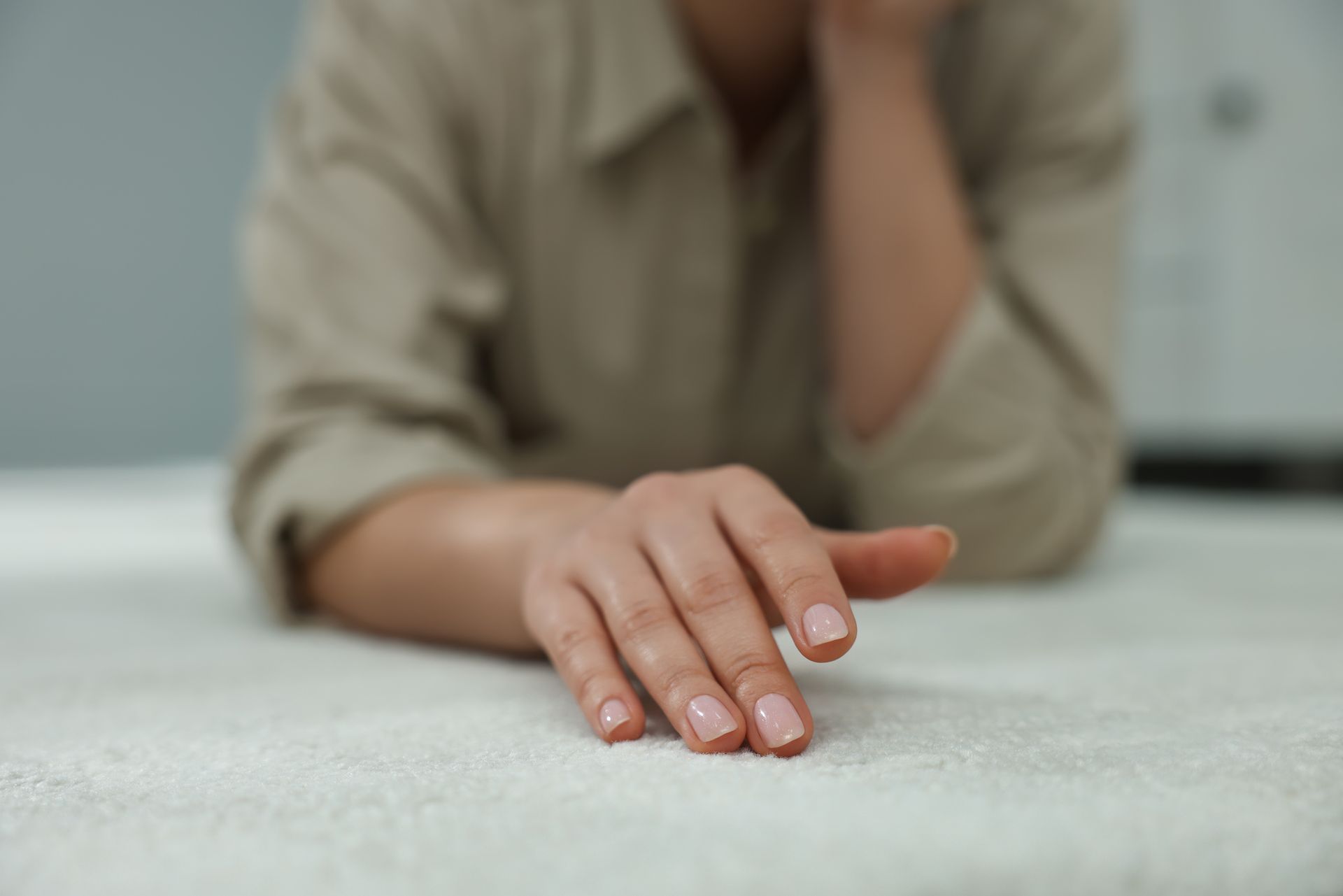 A close-up of a woman touching soft white carpet indoors.