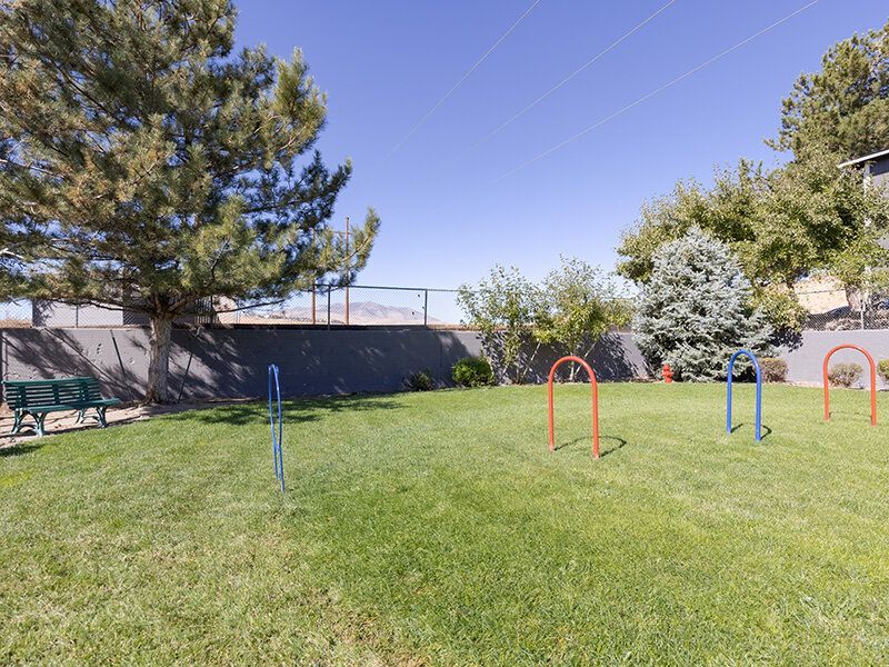Open grassy community area with colorful metal play arches, a bench, and trees.