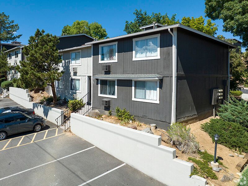 Two-story dark-gray apartment building with white-trimmed windows and a parking area.