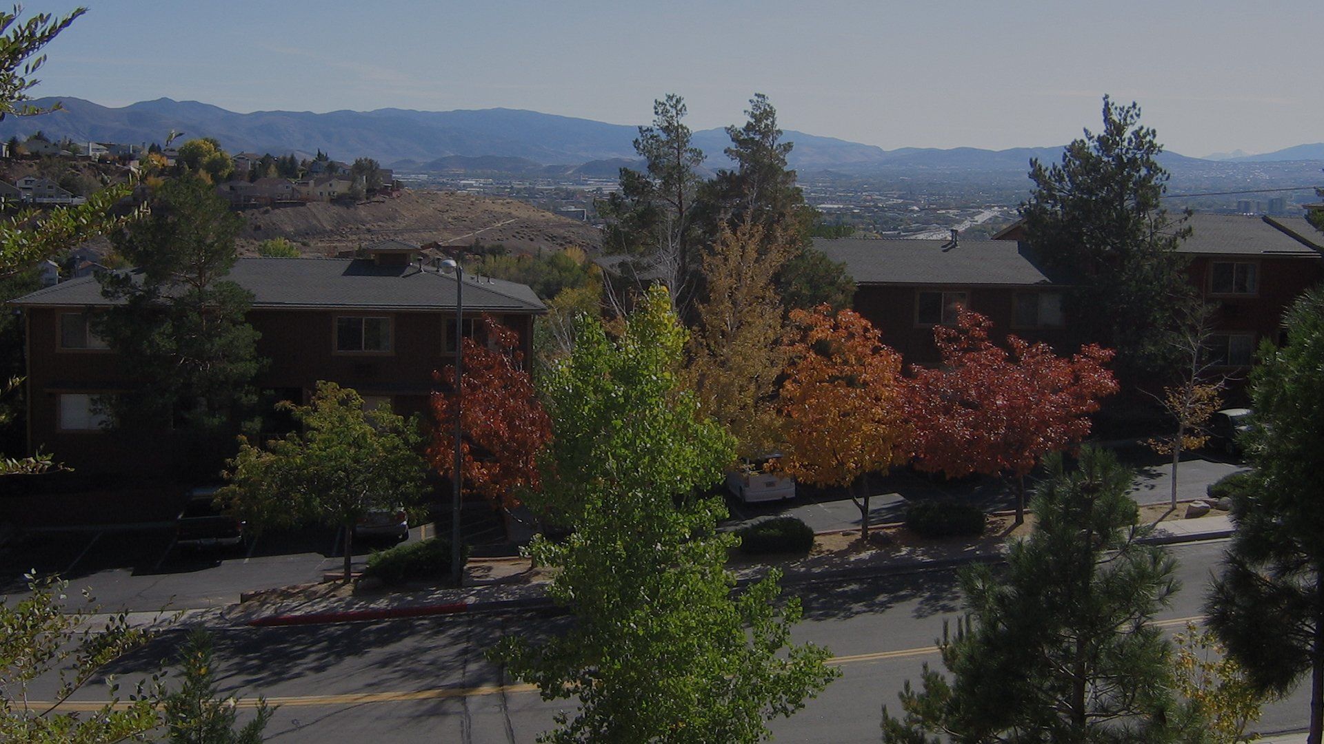 Exterior view of a multi-unit apartment complex with trees and distant hills.