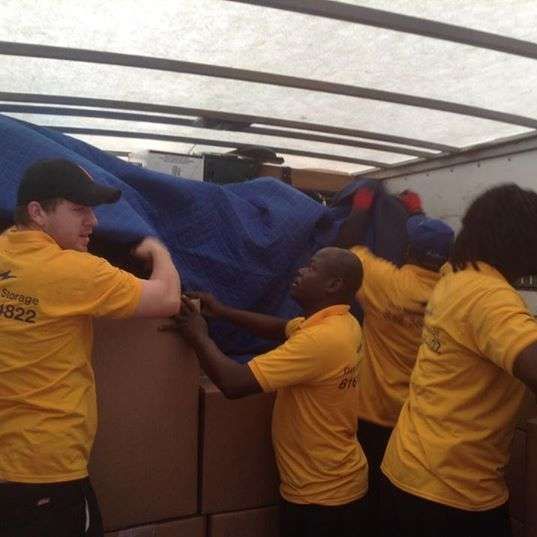 A group of men in yellow shirts are loading boxes into a truck