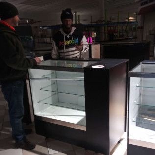 A man wearing a polaroid shirt is standing in front of a glass display case