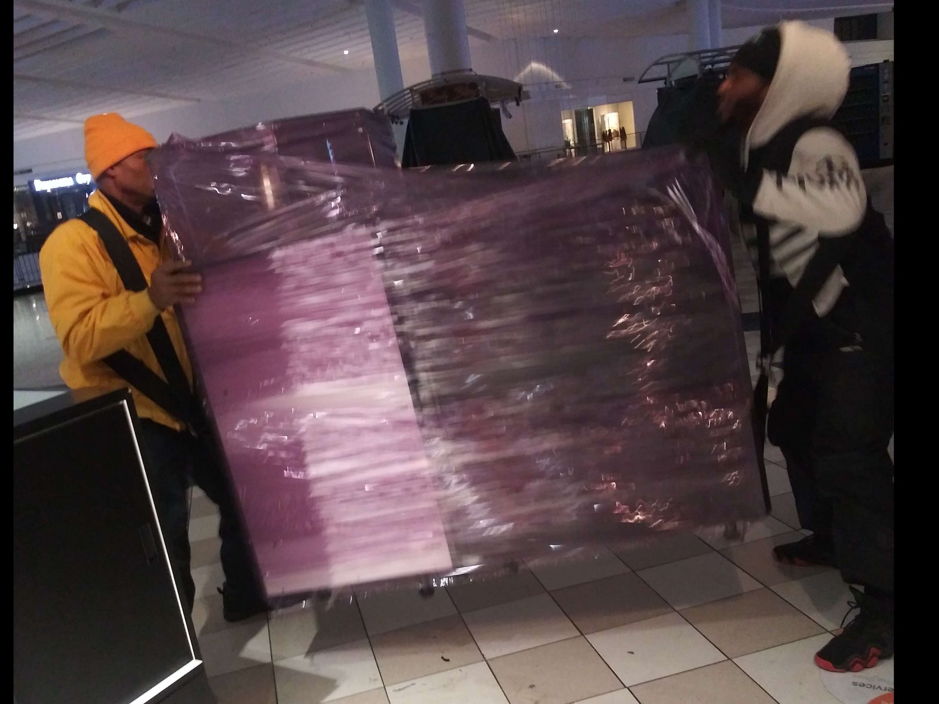 A man in a yellow jacket is carrying a large purple object