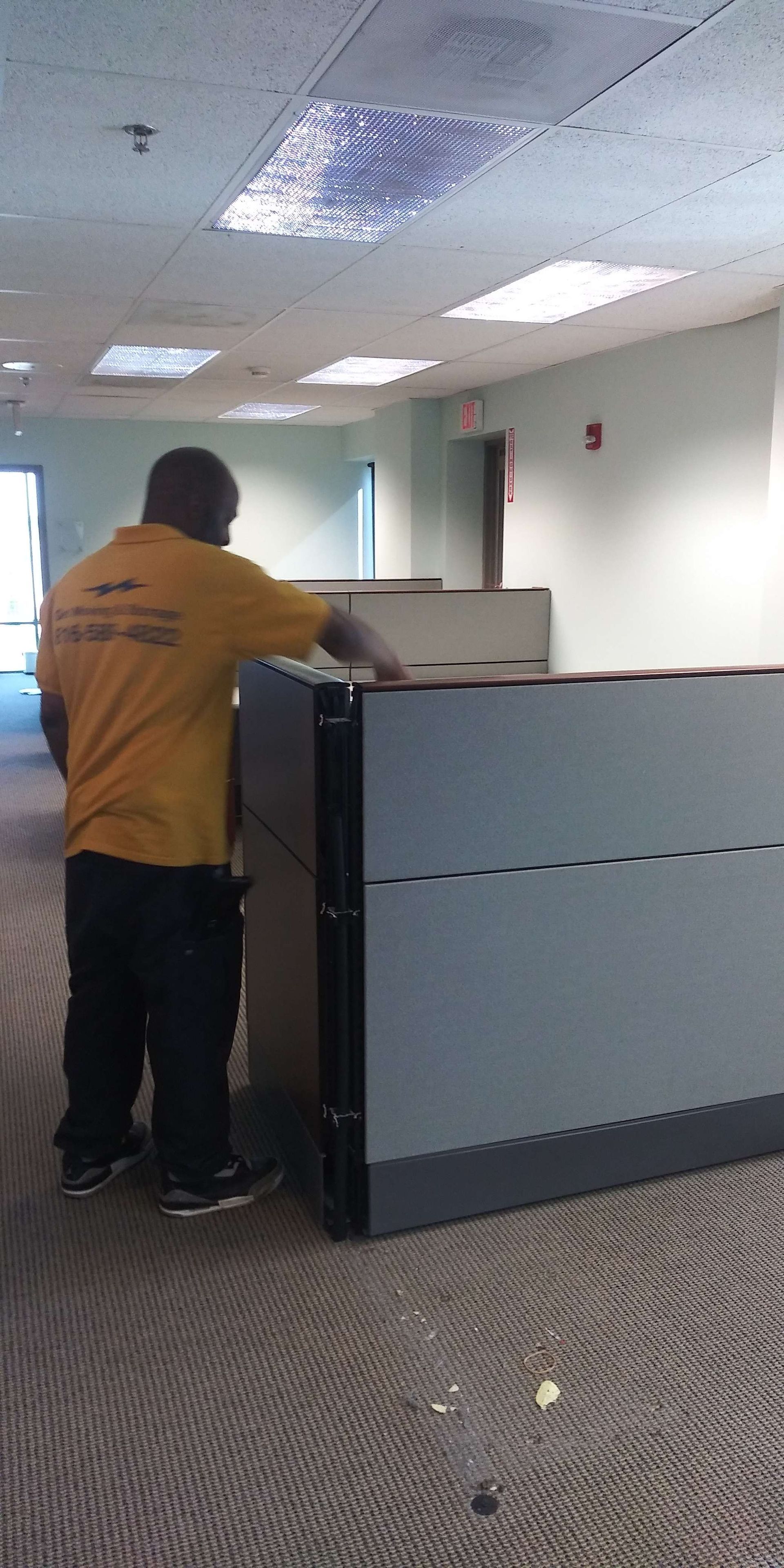 A man in a yellow shirt is standing next to a cubicle in an office.