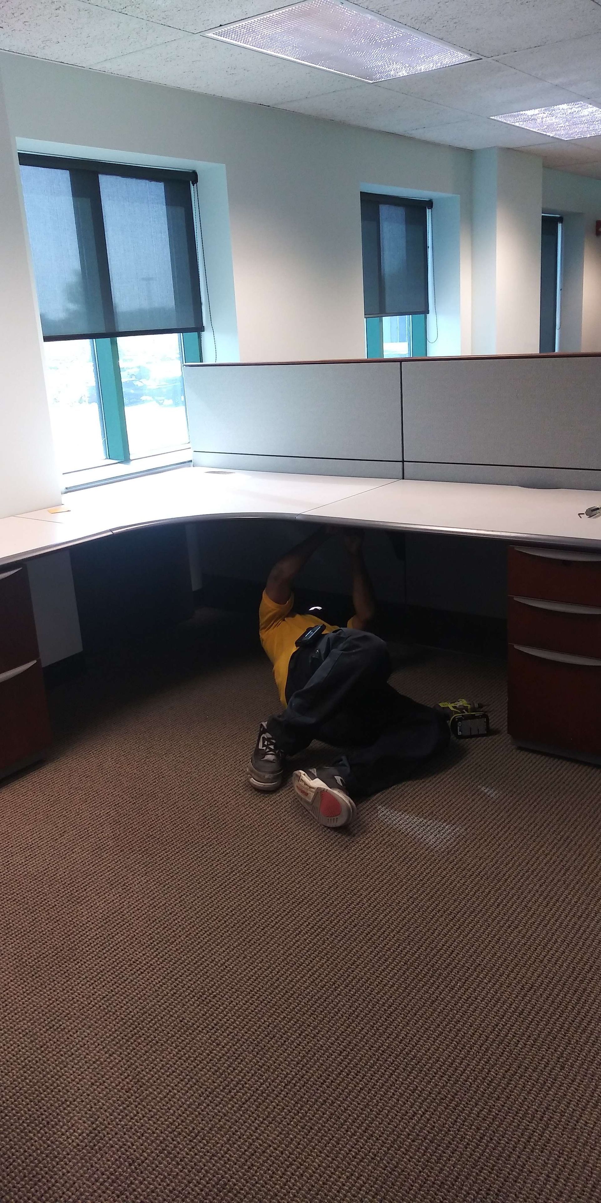 A person is crawling under a desk in an office.