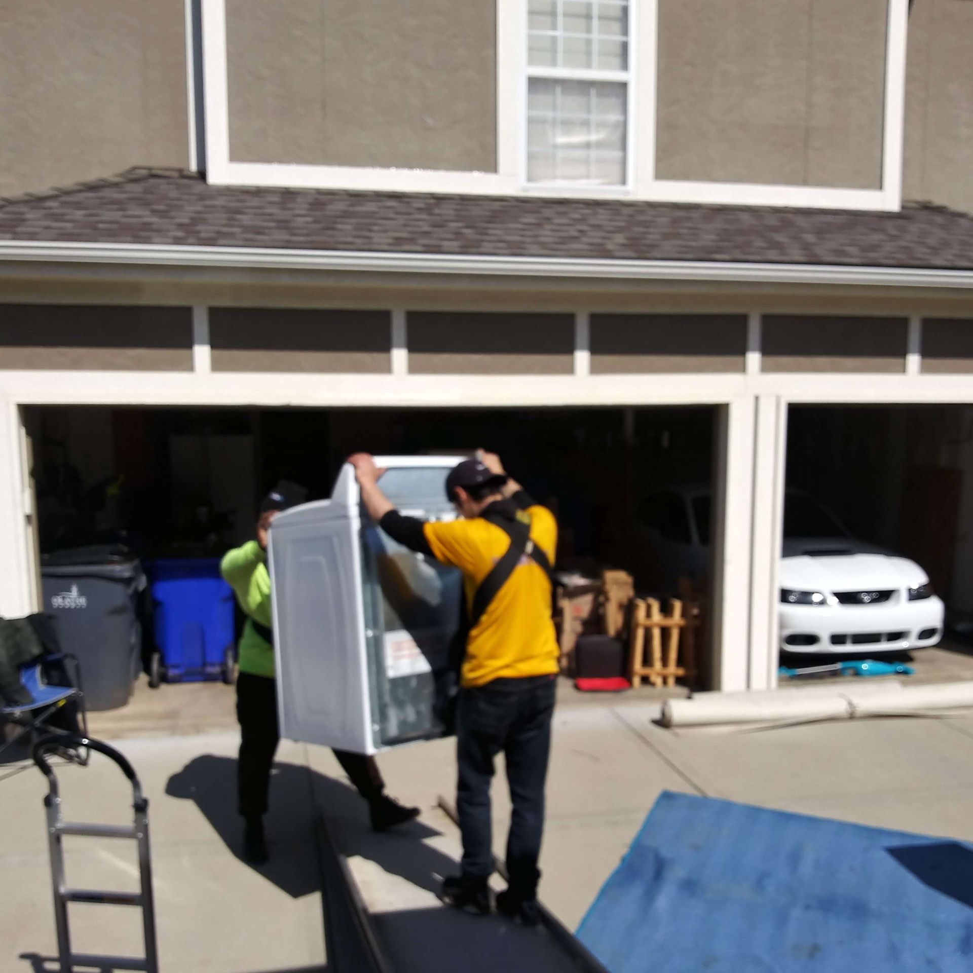 A man in a yellow shirt is carrying a refrigerator