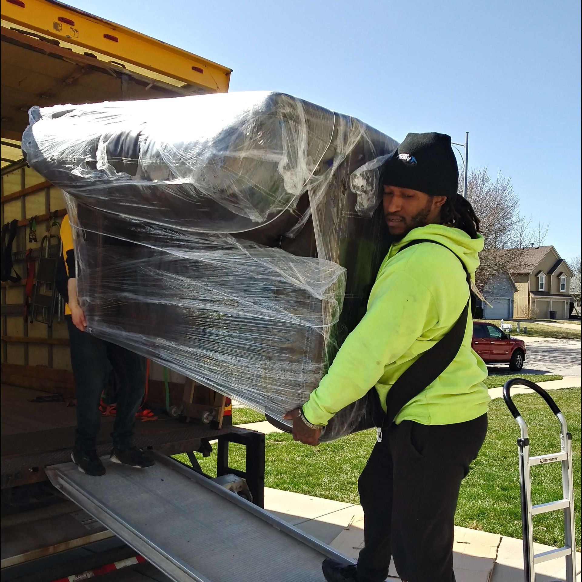 A man in a neon yellow sweatshirt is carrying a large piece of plastic