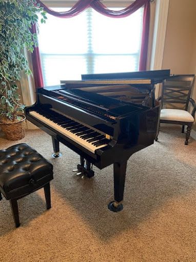 A black grand piano is sitting in a living room next to a window.