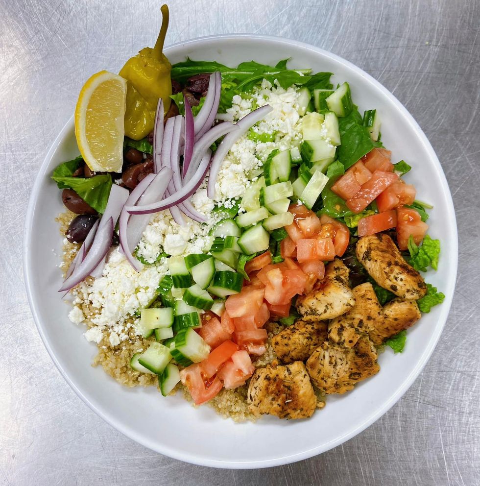 Greek salad bowl with chicken, vegetables, feta cheese, and lemon wedge.