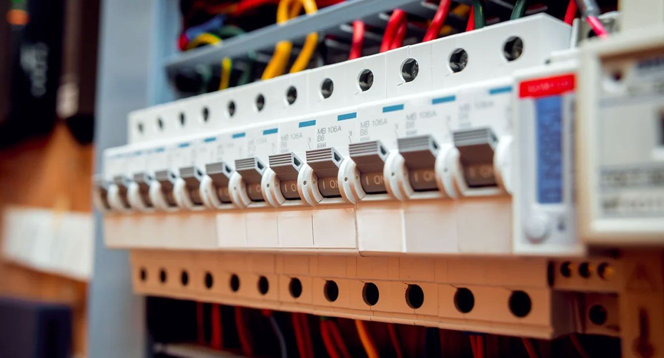 Person using a multimeter to test electrical wiring in a panel.