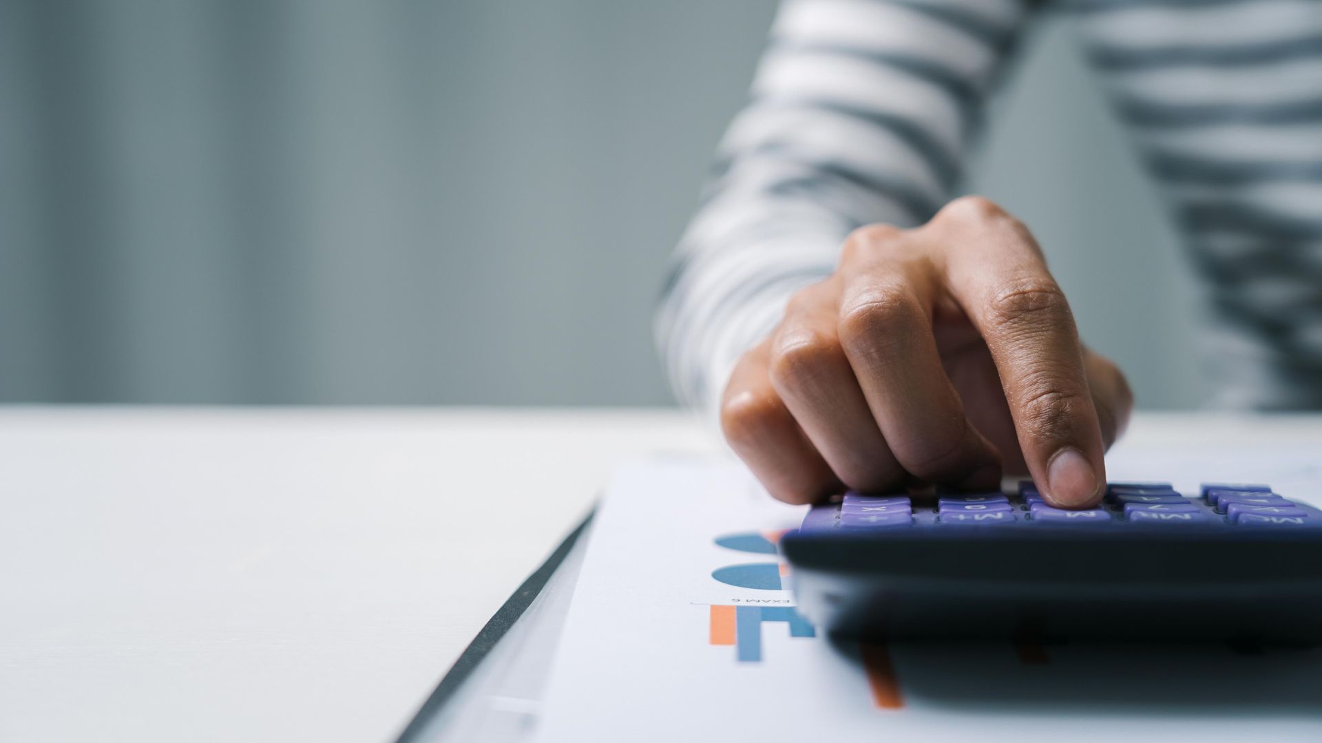 Person's hand using a calculator on a desk with a document.
