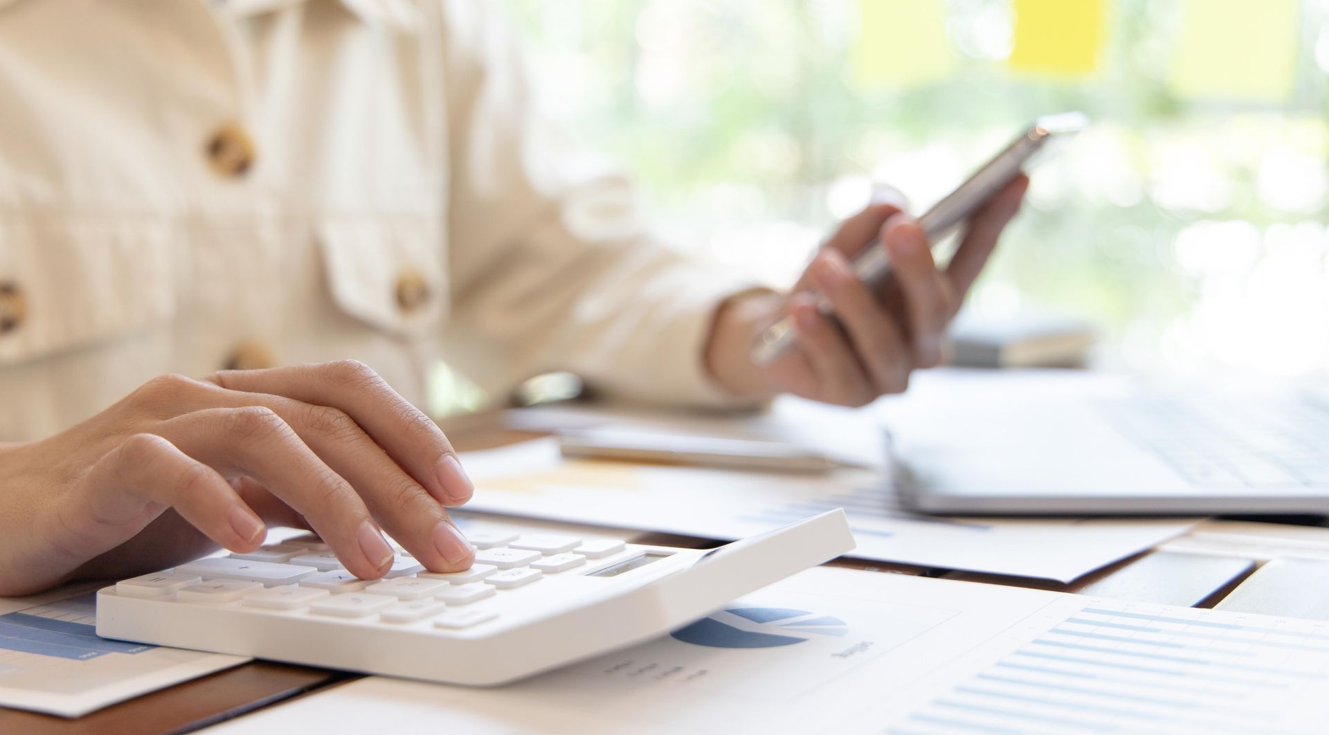 Person using a calculator and smartphone, working on financial documents at a desk.