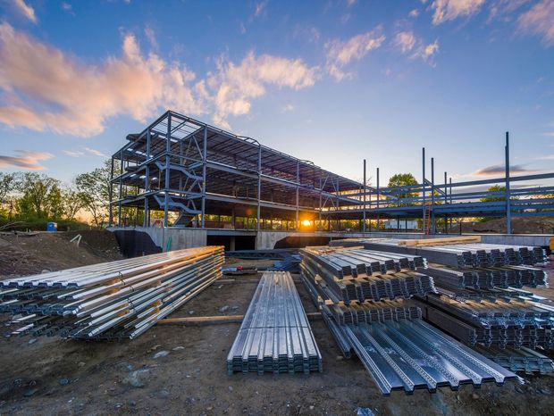 Cantiere edile con travi d'acciaio impilate e una struttura parzialmente costruita al tramonto.