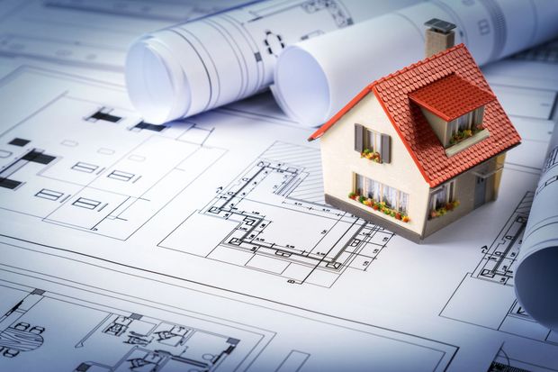 Modello di casa in miniatura su planimetrie architettoniche con piani arrotolati e una penna