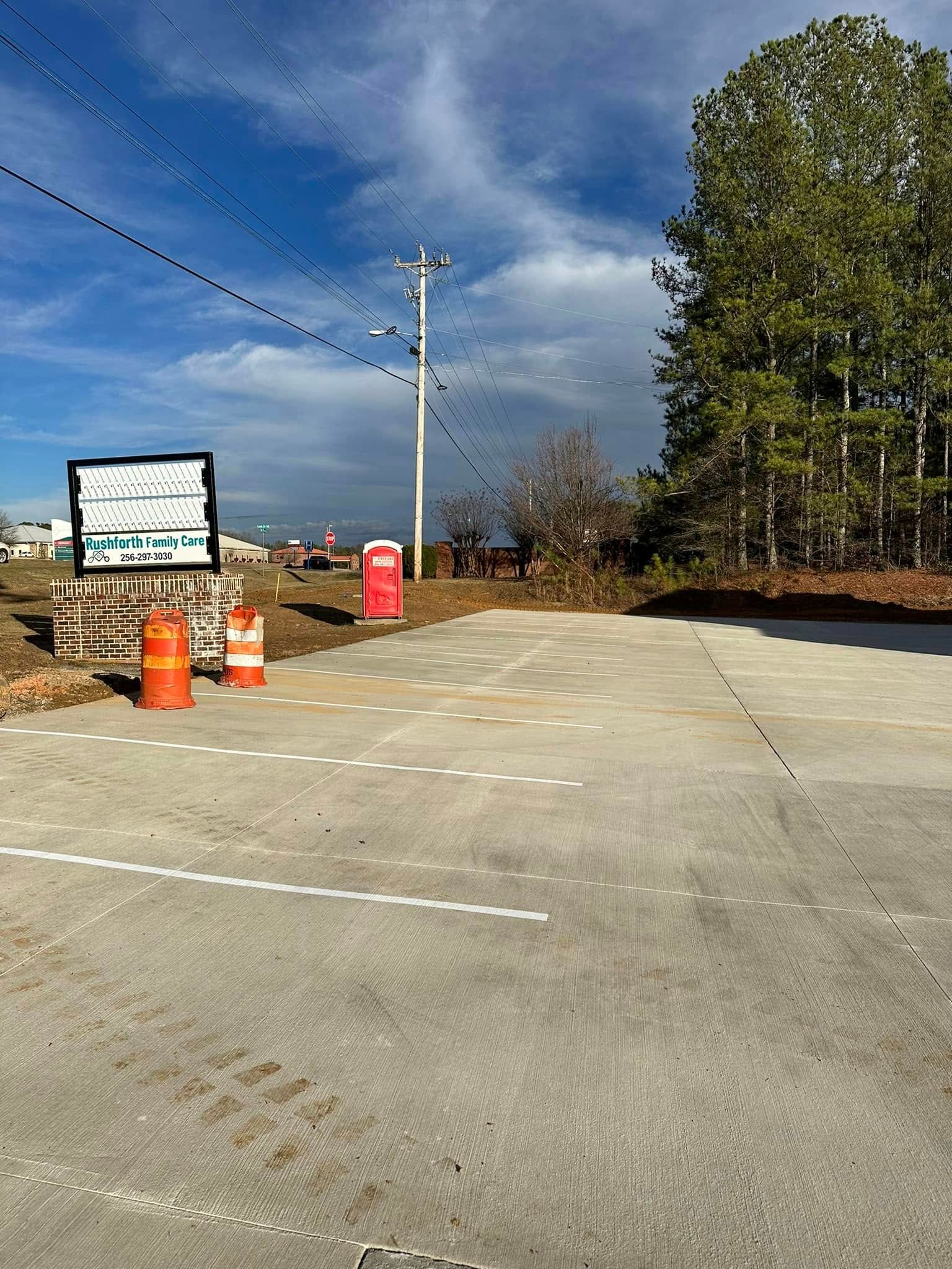 Concrete parking area with construction cones, a sign, and power lines against a cloudy sky.