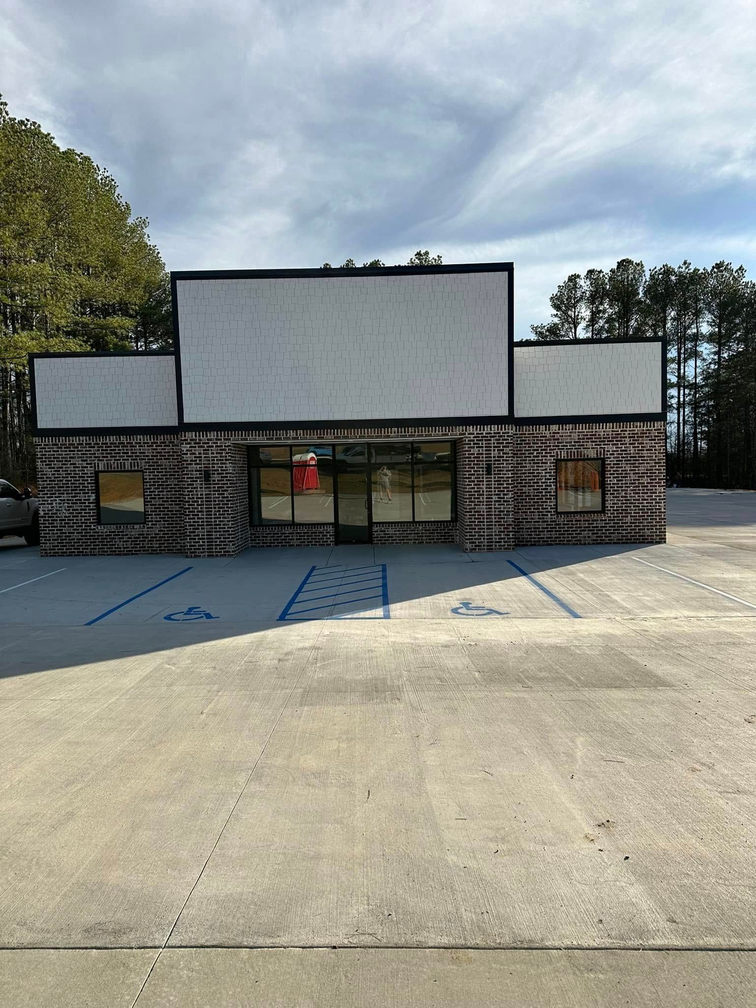 Exterior of a brick building with blank sign panels, glass doors, and parking spaces, under a cloudy sky.