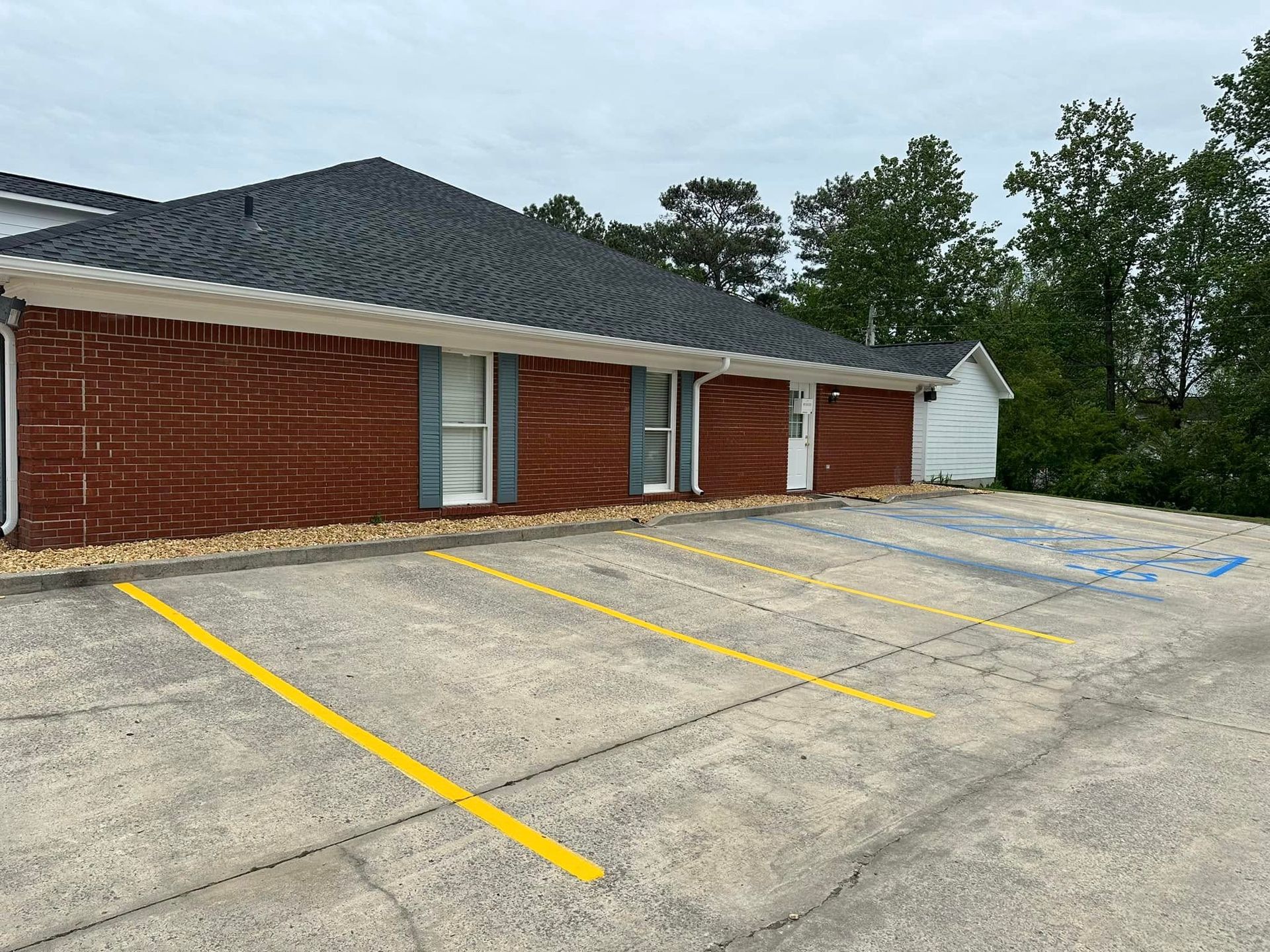 Brick building with yellow parking lines; one handicap space. Trees in the background.