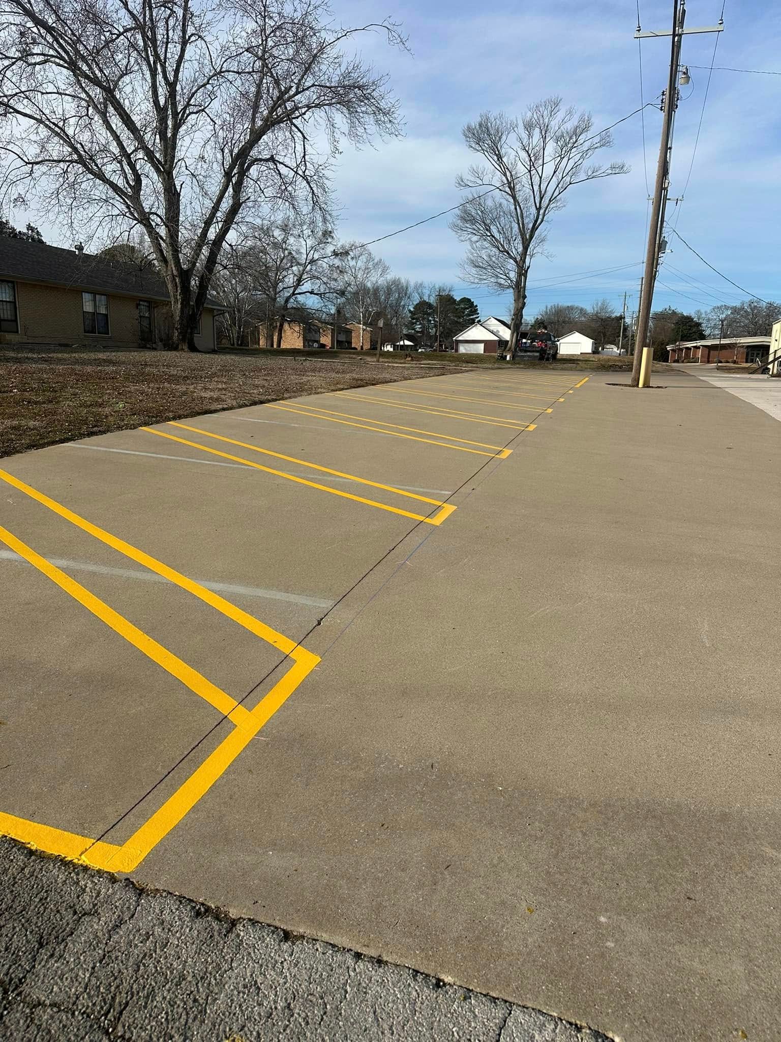 Concrete parking lot with yellow painted lines for parking spaces and a small building in the background.