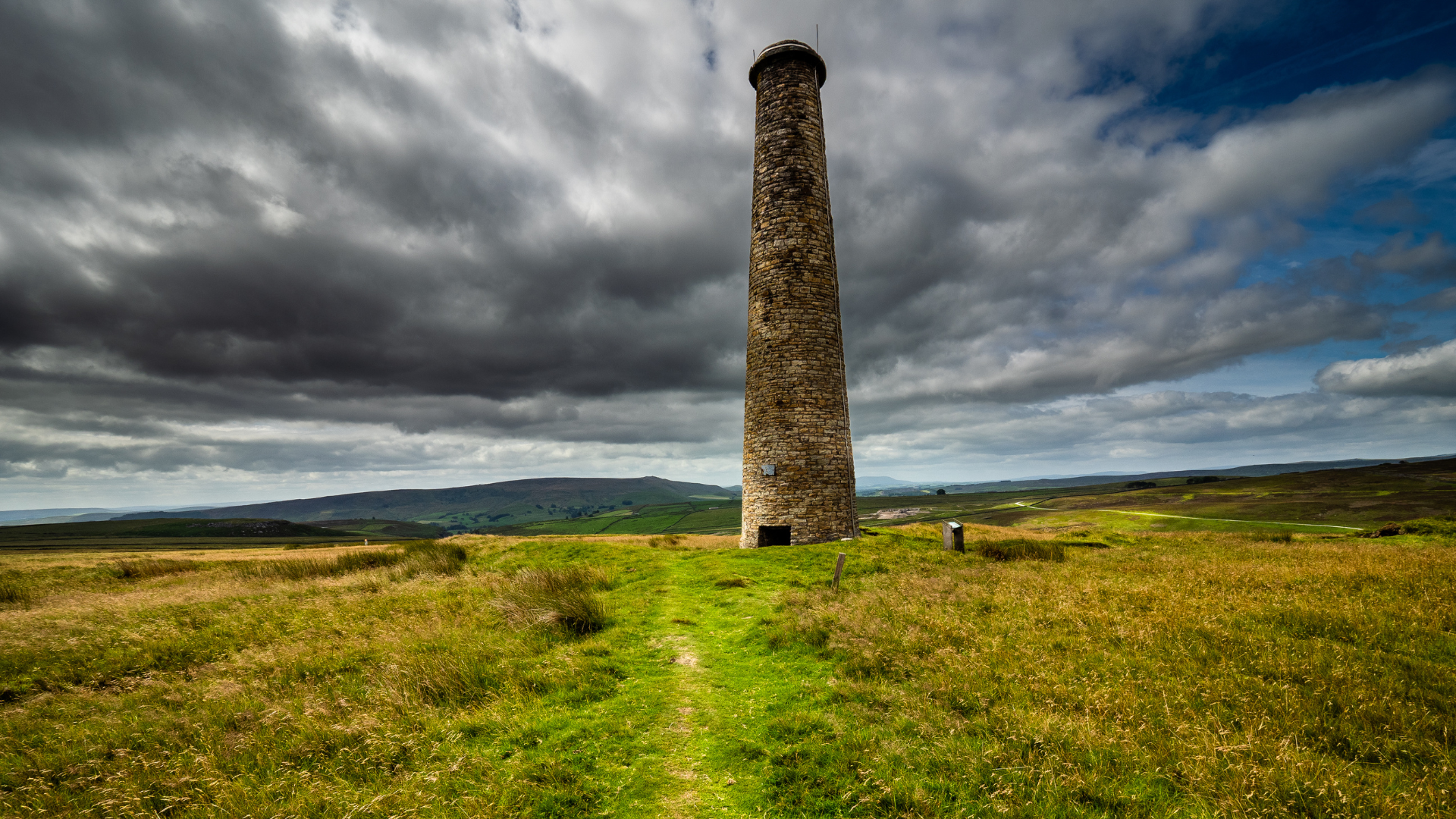 A tall stone tower is sitting in the middle of a grassy field.