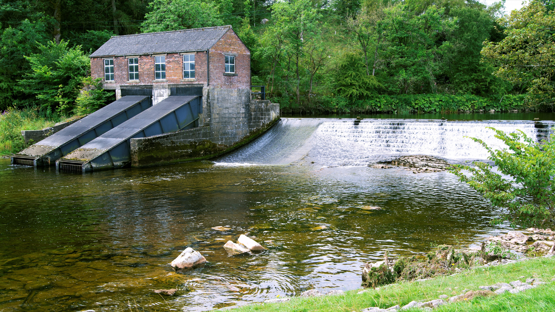 A brick building is sitting next to a river surrounded by trees.