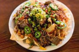 A close up of a plate of nachos on a wooden table.