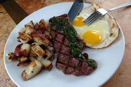 A white plate topped with steak eggs and potatoes