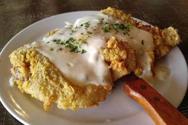 A white plate topped with a piece of fried chicken and gravy.