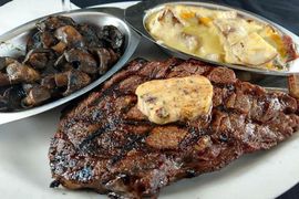 A white plate topped with a steak , mushrooms and mashed potatoes.