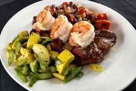 A white plate topped with steak shrimp and vegetables