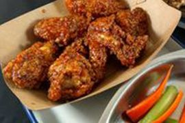 A bowl of chicken wings next to a bowl of carrots and celery.