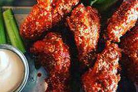 A close up of a plate of chicken wings with celery and dipping sauce.