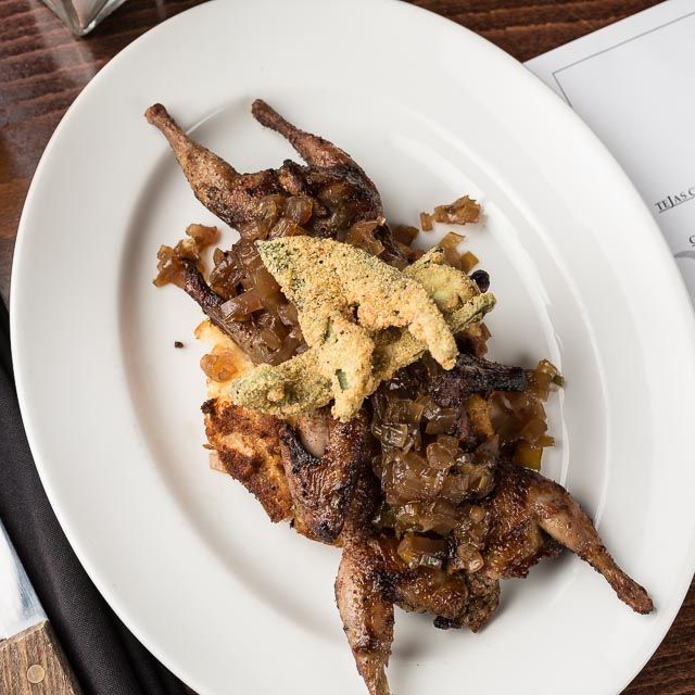 A white plate topped with quail and sauce on a table