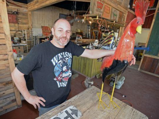 A man wearing a wilson shirt stands next to a statue of a rooster