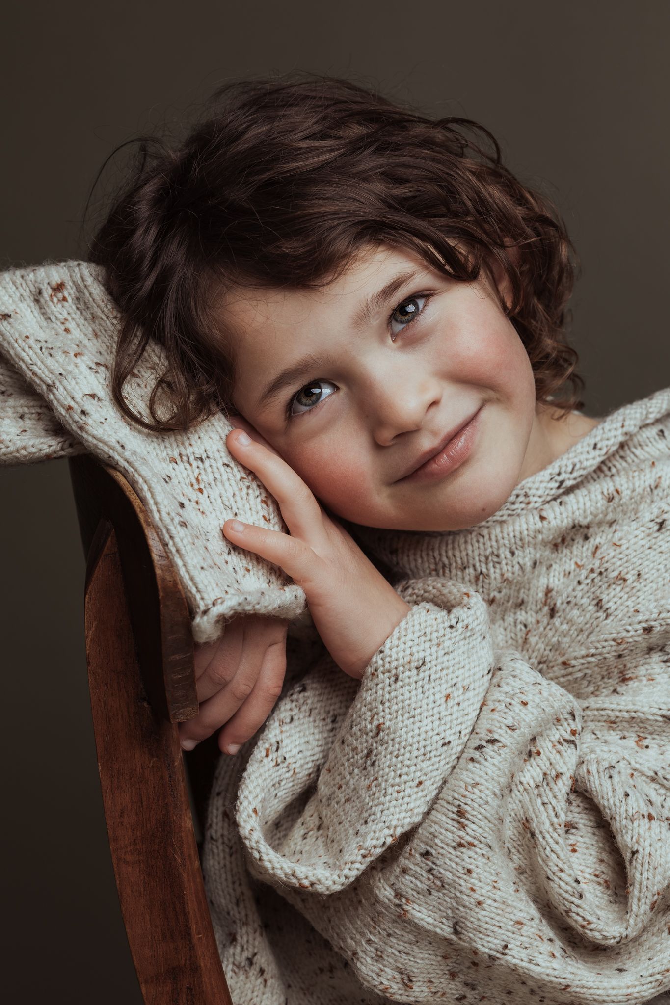 Sibbe kinderportret Portret van een meisje op een stoel dat dromerig naar boven kijkt.