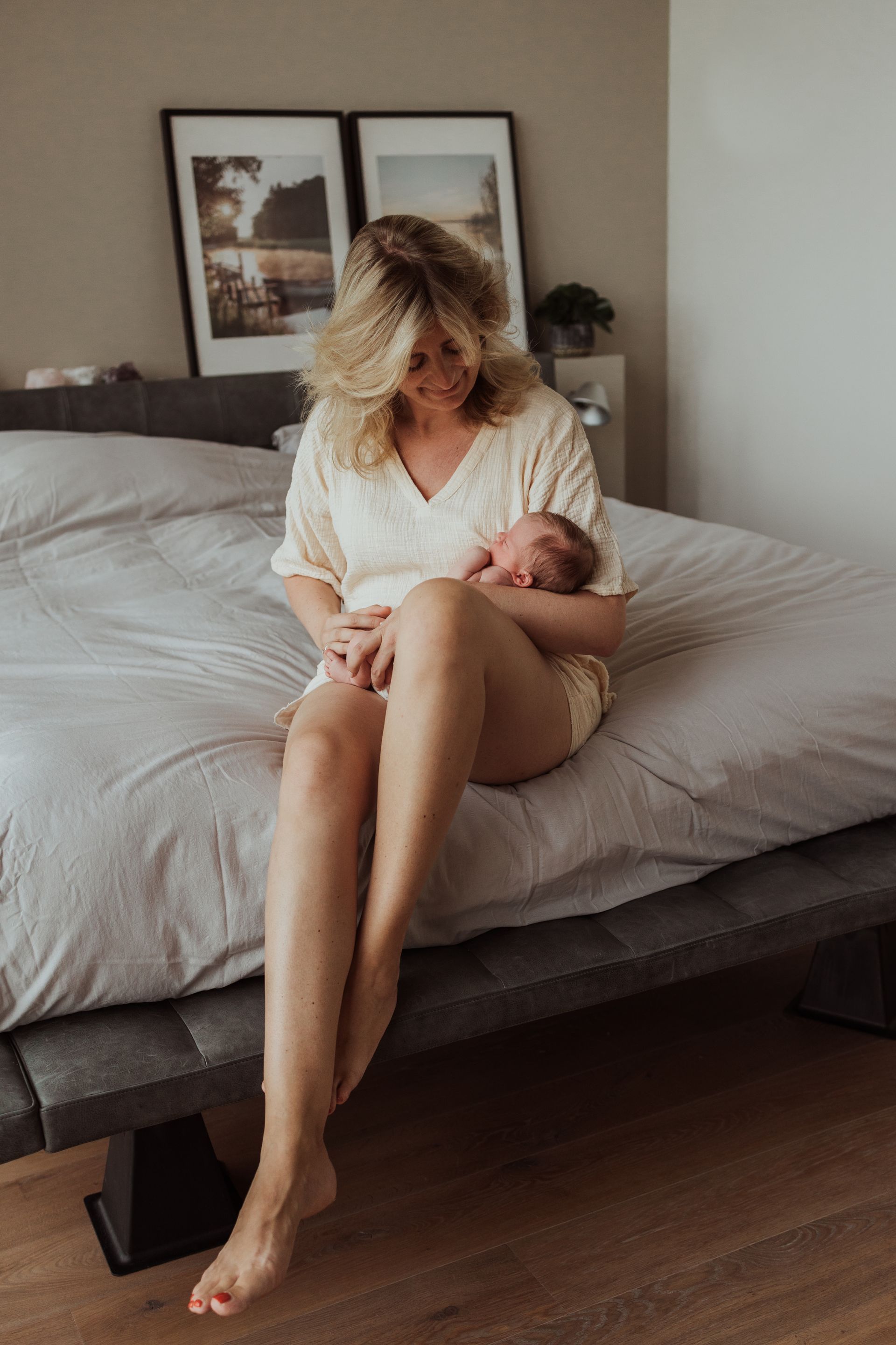 Een vrouw zit op een bed met een pasgeboren baby in haar armen.