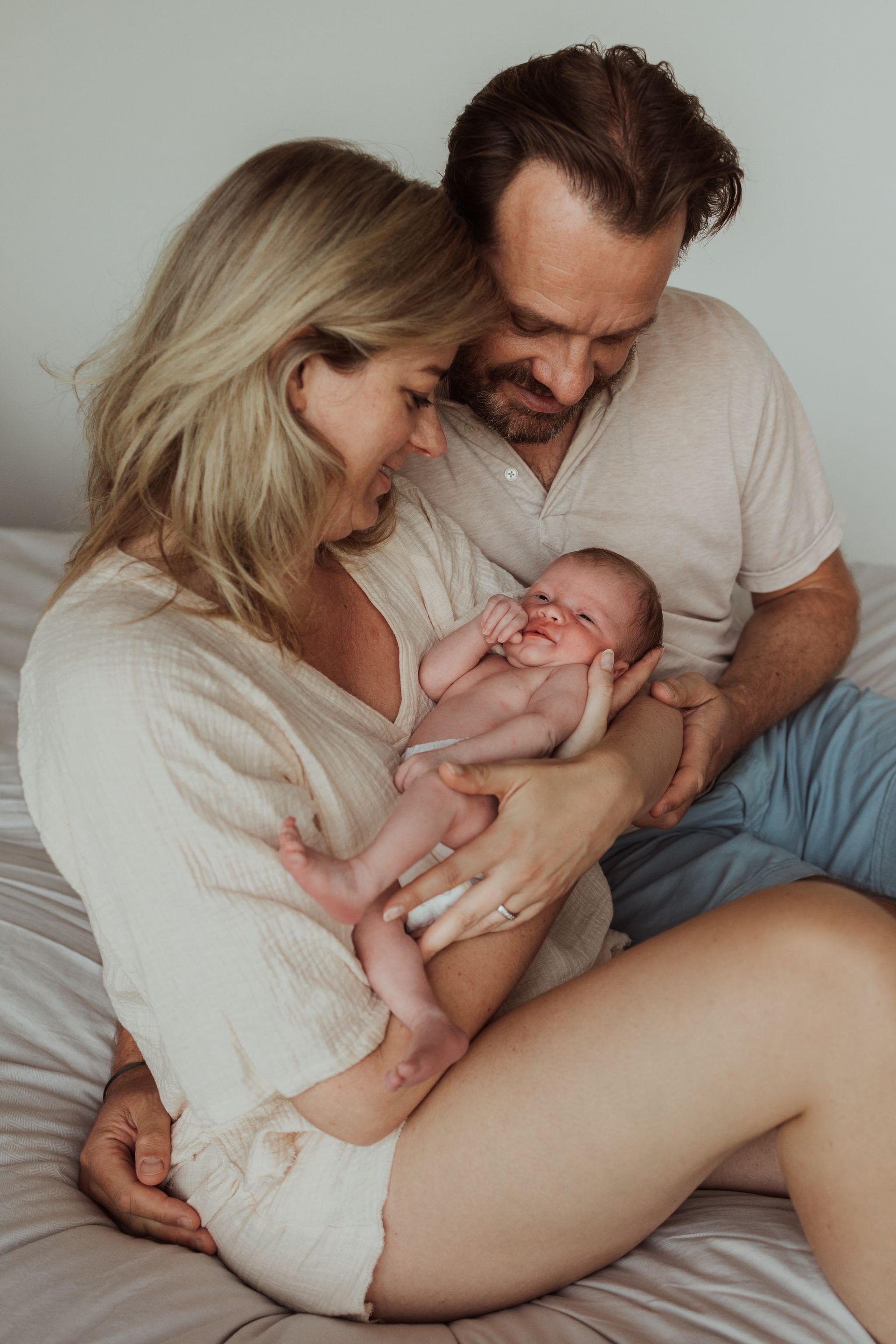 Een man en een vrouw houden een pasgeboren baby op een bed vast.