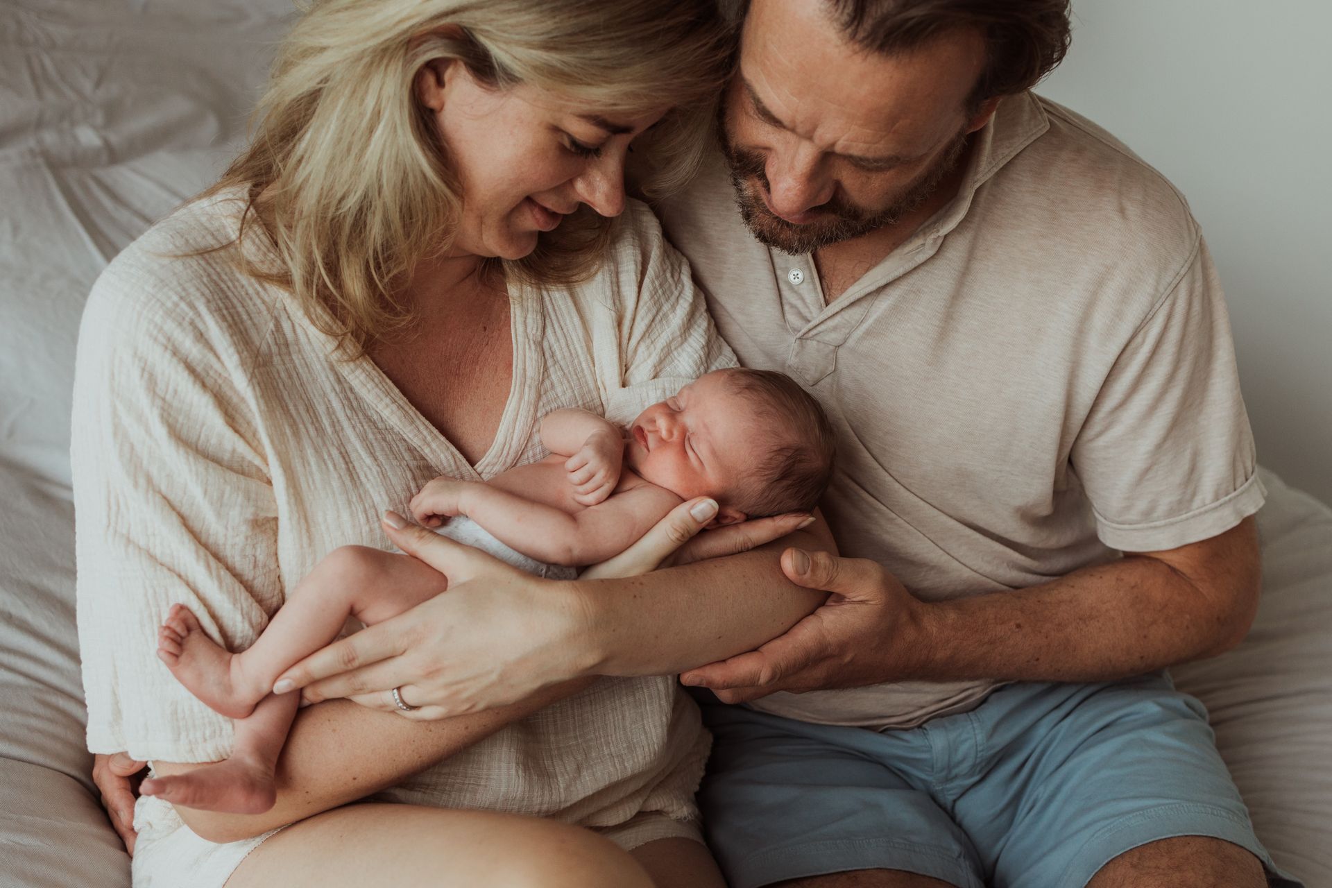 Een man en een vrouw zitten op een bed met een pasgeboren baby.